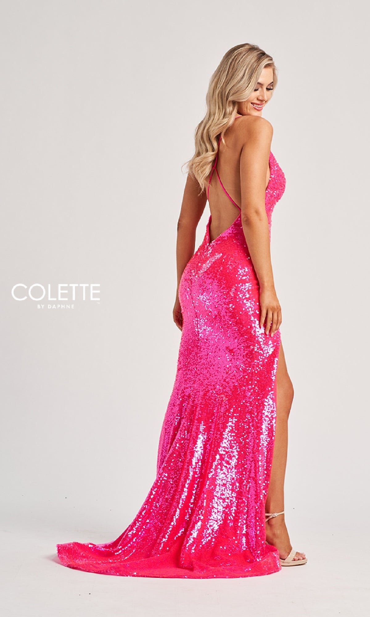 A woman poses sideways against a plain background wearing the Colette CL8070, a long, bright pink sequined prom dress featuring a backless design and thigh-high slit.